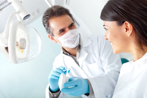 Dentist showing a woman how to brush her teeth on prosthesis